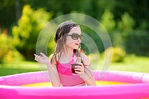 Adorable little girl playing in inflatable baby pool. Happy kid splashing in colorful garden play center on hot summer day.