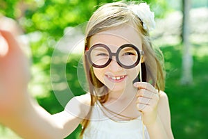 Adorable little girl playing with paper glasses on a stick