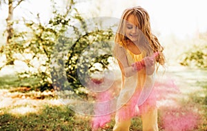Adorable little girl playing in the park with magical pink dust for an imagination or fairy tale concept. Happy child smiling