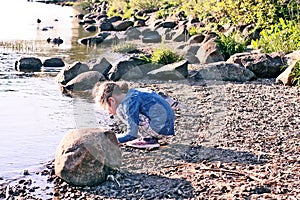 Adorable little girl playing with small stones on the river coast at spring.