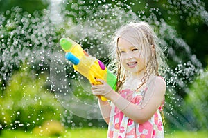Adorable little girl playing with water gun on hot summer day. Cute child having fun with water outdoors.