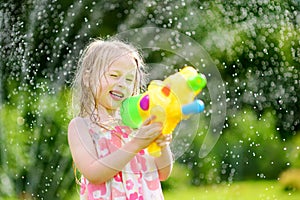 Adorable little girl playing with water gun on hot summer day. Cute child having fun with water outdoors.