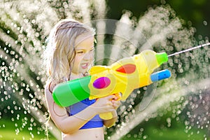 Adorable little girl playing with water gun on hot summer day. Cute child having fun with water outdoors.