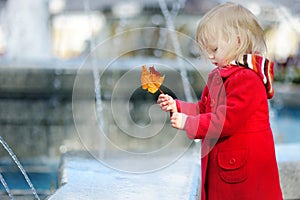 Adorable little girl playing with yellow autumn leaf