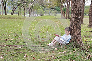 Adorable little girl reading a book sitting under a tree outdoor garden