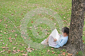 Adorable little girl reading a book sitting under a tree outdoor garden