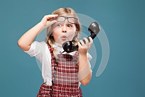 Adorable little girl in red dress, white shirt and glasses holds phone handset