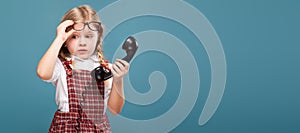 Adorable little girl in red dress, white shirt and glasses holds phone handset