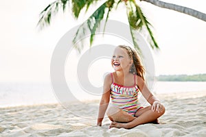 Adorable little girl relax on sandy beach under palm tree with copy space