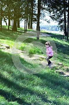 Adorable little girl runs up the wooden stairs in the forest. Sunny day