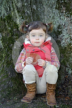 Adorable little girl seated against a tree