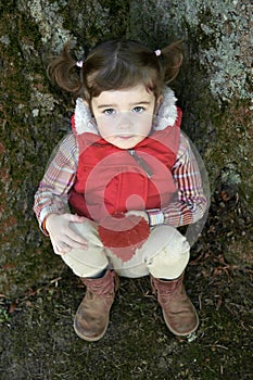 Adorable little girl seated against a tree looking up