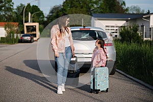 Adorable little girl sits on her kid suitcase and waiting for the trip with her mom. Two beautiful girls prepare