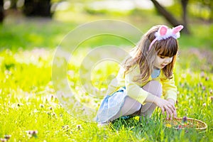 Adorable little girl sitting at the green grass playing in the garden on Easter egg hunt