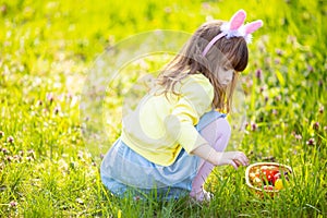 Adorable little girl sitting at the green grass playing in the garden on Easter egg hunt