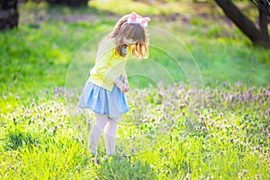 Adorable little girl sitting at the green grass playing in the garden on Easter egg hunt