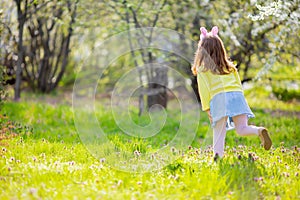 Adorable little girl sitting at the green grass playing in the garden on Easter egg hunt