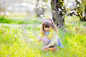 Adorable little girl sitting at the green grass playing in the garden on Easter egg hunt