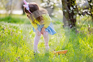 Adorable little girl sitting at the green grass playing in the garden on Easter egg hunt