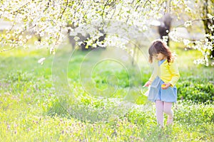 Adorable little girl sitting at the green grass playing in the garden on Easter egg hunt