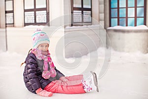 Adorable little girl sitting on ice with skates