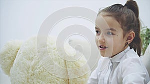 Adorable little girl sitting on the sofa, talking with her teddy.