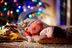 Adorable little girl sleeping under the Christmas tree by a fireplace