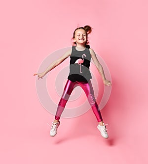 Adorable little girl in sleeveless t-shirt with flamingo and bright rose leggings is merrily jumping on place. photo