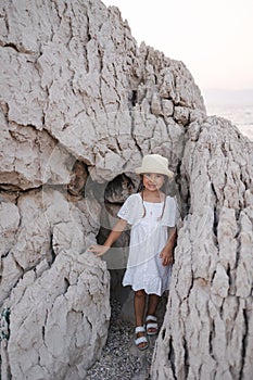 Adorable little girl stand between the rocks and peeking out to camera