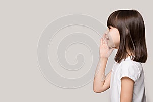 Adorable little girl standing aside, holding hand near mouth. photo