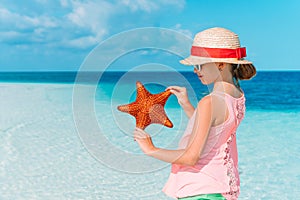 Adorable little girl with starfish on white empty beach