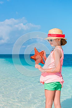 Adorable little girl with starfish on white empty beach
