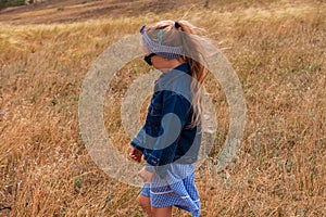 Adorable little girl in a straw hat, blue plaid summer dress in grass field countryside. Child with long blonde braid