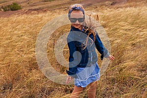 Adorable little girl in a straw hat, blue plaid summer dress in grass field countryside. Child with long blonde braid