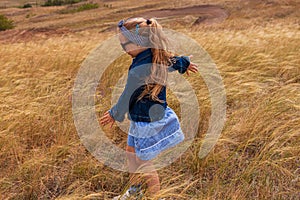 Adorable little girl in a straw hat, blue plaid summer dress in grass field countryside. Child with long blonde braid