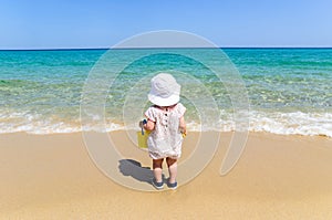 Adorable little girl in swimsuit having fun at tropical sandy beach