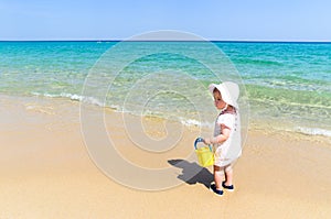 Adorable little girl in swimsuit having fun at tropical sandy beach