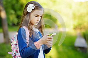 Adorable little girl taking a photo with a smartphone on beautiful summer day