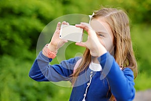 Adorable little girl taking a photo with a smartphone on beautiful summer day