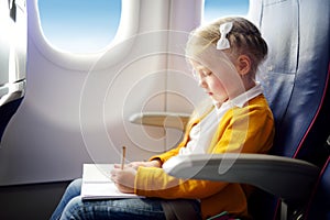Adorable little girl traveling by an airplane. Child sitting by aircraft window and drawing a picture with colorful pencils. Trave