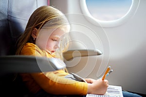 Adorable little girl traveling by an airplane. Child sitting by aircraft window and drawing a picture with felt-tip pens.