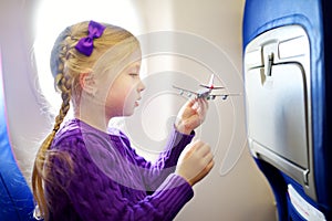 Adorable little girl traveling by an airplane. Child sitting by aircraft window and playing with toy plane. Traveling with kids.