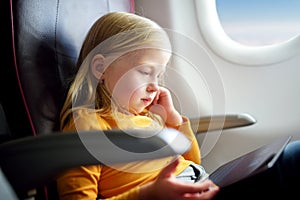 Adorable little girl traveling by an airplane. Child sitting by aircraft window and using a digital tablet