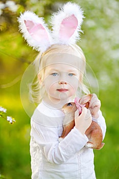 Adorable little girl wearing bunny ears in blooming cherry garden on spring day