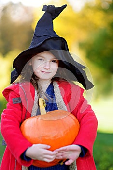 Adorable little girl wearing halloween costume having fun on a pumpkin patch