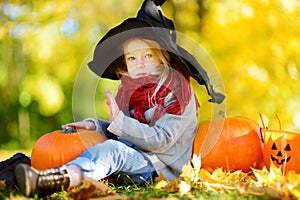 Adorable little girl wearing halloween costume having fun on a pumpkin patch on autumn day