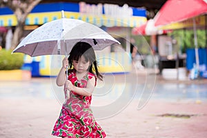 Adorable little girl wearing a red dress with watermelon prints walks an umbrella on a drizzly day in the rainy season.