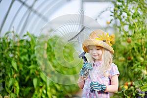 Adorable little girl wearing straw hat and childrens garden gloves playing with her toy garden tools in a greenhouse