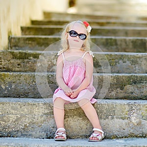 Adorable little girl wearing sunglasses sitting on stairs