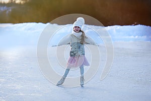 Adorable little girl in the white clothes and hat on the ice rink